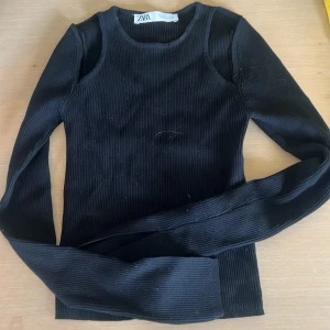 Svart ribbad långärmad topp Zara - Svart ribbad långärmad topp från Zara med tight passform. Tröjan har rund halsringning och är tillverkad i ett stretchigt material som sitter snyggt på kroppen. Perfekt att styla med jeans eller kjol för en clean look.