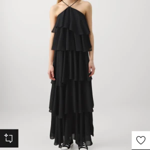 Svart volangklänning med smala axelband - Snygg svart långklänning med flera lager volanger och smala axelband som korsas i nacken. Klänningen har en luftig och flowy känsla, perfekt för dig som vill sticka ut med en cool och elegant stil.