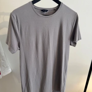 Grå basic t-shirt från Riley - Enkel och stilren grå t-shirt från Riley med rund halsringning och korta ärmar. Tillverkad i mjuk bomull som känns skön mot huden. Perfekt för en clean och avslappnad look.