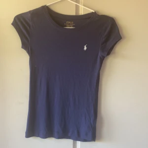 Marinblå t-shirt  - Snygg marinblå t-shirt från Polo Ralph Lauren med klassisk vit logga broderad på bröstet. på lappen står storleken 8-10år men skulle påstå att den sitter som en xs .