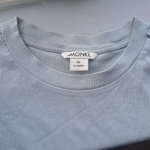 Ljusblå ribbad topp  - Säljer en ljusblå ribbad topp från Monki i storlek XS. T-shirten har korta ärmar, rund halsringning.
