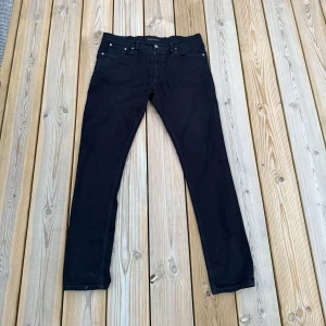 Svarta jeans från Nudie Jeans Co - Säljer ett par svarta jeans från Nudie Jeans Co i klassisk femficksmodell. Jeansen har smal passform och raka ben, tillverkade i slitstarkt bomullstyg. Snygga detaljer med svarta sömmar och diskret logga på insidan.