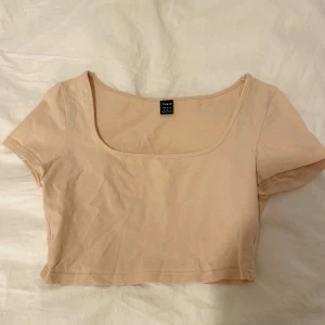 Beige croppad topp från SHEIN - En enkel och stilren croppad topp från SHEIN i beige i storlek S. Toppen har korta ärmar, rundad djup urringning och är tillverkad i mjuk bomull. Perfekt att matcha med höga jeans eller kjol för en clean look.