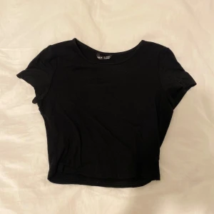 Svart croppad topp från SHEIN - Enkel och stilren svart croppad topp från SHEIN i storlek S. Modellen har rund halsringning och korta ärmar, perfekt att matcha med jeans eller kjol. Tunn och mjuk i materialet, passar dig som gillar minimalistisk stil.