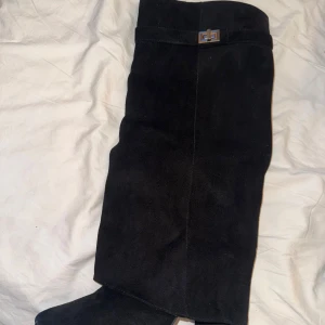 Svarta mockastövlar med gulddetalj - Snygga svarta stövlar i mocka med spetsig tå och guldfärgad spänndetalj upptill. Stövlarna har dragkedja på insidan.