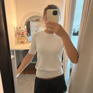 Vit stickad kortärmad tröja - Säljer en enkel och stilren vit stickad tröja med korta ärmar och rund hals. Tröjan har en mjuk och bekväm passform som sitter snyggt på kroppen. Perfekt att matcha med både jeans och kjol för en clean look.