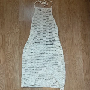 Creamvit virkad strand klänning  - Superfin creamvit virkad strand klänning med halterneck och knyt i nacken och rygg. Klänningen är kort och har öppen rygg