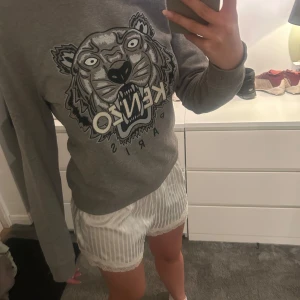 Grå Kenzo sweatshirt med tigertryck - Säljer en grå sweatshirt från Kenzo med ikoniskt broderat tigerhuvud och logga på bröstet. Tröjan har rund hals, långa ärmar och är gjord i mjuk bomullsmix. Perfekt statement-piece för dig som gillar streetstyle och vill sticka ut.