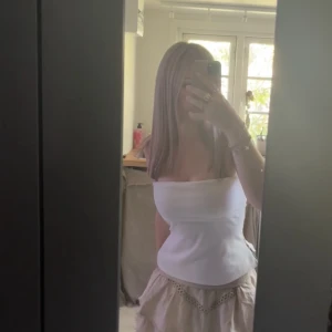 Vit bandeau tubtopp med dragkedja - Säljer en vit bandeau tubtopp med tight passform och dragkedja i sidan. Toppen är axelbandslös och har en stilren, enkel look som passar perfekt till sommaren. Materialet känns mjukt och följsamt mot kroppen. Perfekt för dig som gillar minimalistisk stil.