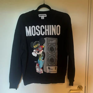 Svart Moschino x H&M tröja med Mickey Mouse - Cool svart tröja från Moschino x H&M i storlek XS med stort tryck av Mickey Mouse i streetstyle och högtalare på framsidan. MOSCHINO-loggan i silver upptill. Långärmad och i mjuk bomull, perfekt för dig som gillar statement-plagg. Priset är inte hugget i sten, vid snabb affär kan jag halvera priset