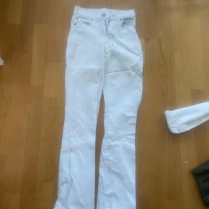 Vita bootcut jeansbyxor - Säljer ett par vita jeansbyxor med bootcut-snitt och klassisk femficksdesign. Byxorna har hög midja och är tillverkade i ett mjukt bomullsmaterial. Perfekta för dig som vill ha en clean och fräsch look.