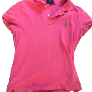Rosa pikétröja från Ralph Lauren - Snygg rosa pikétröja från Ralph Lauren med klassisk krage, korta ärmar och knappar framtill. Tröjan har den ikoniska gröna loggan broderad på bröstet och är gjord i mjuk bomull. Perfekt för en sportig och fräsch look. Storleken är M men passar som S/M. Pris kan diskuteras