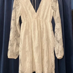 Vit blommig kortklänning Gina Tricot - Superfin vit kortklänning från Gina Tricot med broderade blommor och transparenta långärmar. Djup v-ringning och knytband i nacken ger en romantisk vibe. Perfekt för sommarens alla tillfällen!