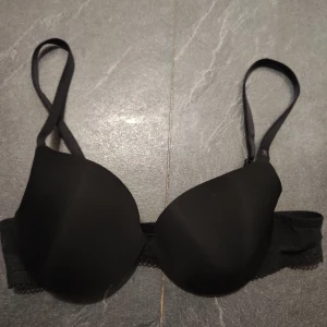 Svart Calvin Klein bh med spetsdetaljer. 70a - Svart bh från Calvin Klein med släta kupor och justerbara axelband. Sidorna har fina spetsdetaljer och diskret mönstrad mesh. Klassisk och stilren design med logga på axelbandet. Perfekt för dig som gillar enkel men snygg underklädesstil. 