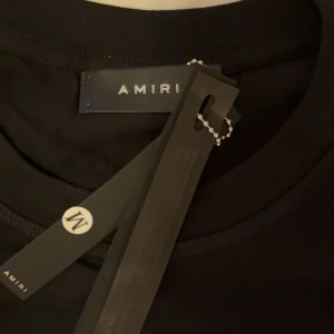 Svart Amiri t-shirt med blått ormmotiv - Svart t-shirt från Amiri med stort tryck av blåa kobror och vit logga på bröstet. Klassisk rund halsringning och korta ärmar. T-shirten har en modern vibe och är tillverkad i mjuk bomull för maximal komfort. storlek M helt ny