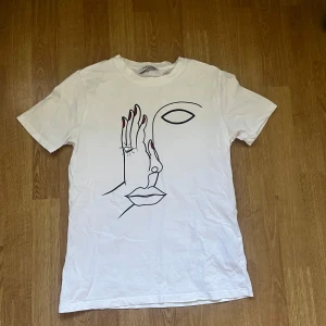 Vit t-shirt med konstmotiv - Vit t-shirt från Pieces med tryck av ett ansikte på framsidan. I stl XS och i superfint skick!