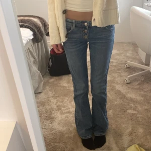 Blå bootcut jeans med knappar - Säljer ett par snygga blå bootcut jeans med flera synliga knappar i gylfen. Jeansen har låg midja och klassisk femficksdesign, jeansen är väldigt stretchiga i sig. Köpta på Gina, storlek 158 tal