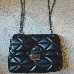 Svart quiltad axelväska med kedja - Svart fin axelväska med kedja- väskan sitter super fint och passar med allt. Med silvrigt lås som fungerar jätte bra- du behöver inte oroa dig för att väskan bara ska öppnas. Lagom mycket utrymme också! 