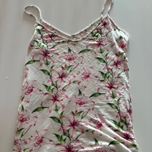 Vit blommig linnetopp med smala band - Ett fint blommigt linne ser likadant ut på fram och bak sida finns ingen storlek då den är avklippen men skulle tro att den är runt M eller L