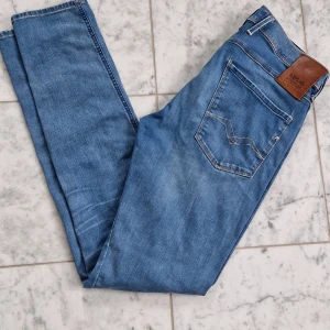 Replay Anbass Hyperflex jeans blå - Säljer ett par Replay Anbass Hyperflex jeans i ljusblå tvätt. Slim fit-modell med klassiska fem fickor, snygga sömmar och läderpatch bak. Jeansen är tillverkade i stretchigt jeansmaterial för extra komfort och rörelsefrihet. Storlek W31 L34