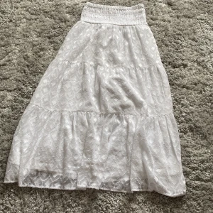 Vit långkjol från Gina Tricot - Superfin vit långkjol från Gina Tricot med ett snyggt mönster. Tyget är lätt och flowy, perfekt för varma sommar dagar. Säljer pågrund av att den är för kort på mig. Har en fläck som syns på sista bilden.
