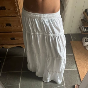 Vit långkjol med volanger - Jättegullig långkjol som knappt är använd. Passar som någon som är ungefär 165 cm. Har inga tecken på användling och är i etg väldigt härligt tyg. Köpt i nepal därför har nog inte så många en lika dan så den blir lite unik.❣️❣️❣️pris kan diskuteras