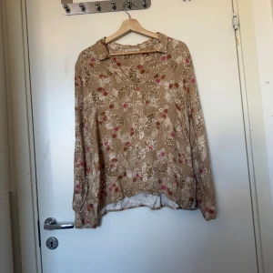 Beige blommig skjorta Odd Molly - Supersöt guld blus med blommigt mönster i vitt, rosa och brunt. Skjortan har v-ringning, krage och långa ärmar. Perfekt för dig som gillar en avslappnad men ändå snygg stil. Från märket Odd Molly i storlek 2 som enligt deras storleksguide motsvarar en storlek M. Mycket fint skick, jag hittar inga synlig anmärkningar eller defekter.  