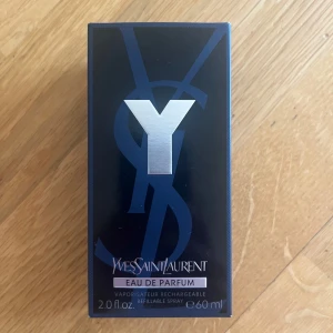 Yves Saint Laurent Y Eau de Parfum 60ml - Y Eau de Parfum från Yves Saint Laurent i en stilren, mörkblå och svart glasflaska med silverdetaljer. Förpackningen är öppnad men perfymen är helt oanvänd. Flaskan rymmer 60 ml och har en robust, maskulin design med metallisk logotyp på framsidan. Parfymen är en påfyllningsbar spray. 