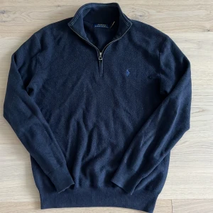 Mörkblå half zip tröja Polo Ralph Lauren - Mörkblå stickad tröja från Polo Ralph Lauren med half zip och broderad logga på bröstet. Tröjan har hög krage och långa ärmar, perfekt för lager-på-lager. Klassisk och stilren design som funkar till det mesta.