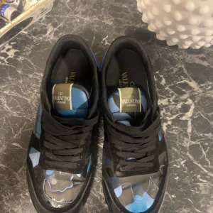Valentino Garavani Rockrunner sneakers - Snygga Valentino Garavani Rockrunner sneakers med svart och blått camouflagemönster. Skorna har svarta snören, detaljer i mocka och skinn samt coola nitar på sulan. Perfekta för dig som vill sticka ut med exklusiva och trendiga sneakers. Andvända max 2 veckor 