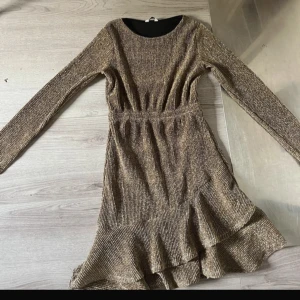 Glittrig guldig klänning med volang - Supersnygg glittrig guldig klänning med långa ärmar och volang nertill.  Knappt använd 