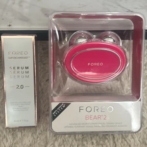 FOREO Bear 2 & Supercharged Serum - Säljer ett FOREO Bear 2 ansiktsverktyg i stark rosa med silverdetaljer, perfekt för microcurrent-behandlingar. Medföljer FOREO Supercharged Serum 2.0, 30 ml, i snygg förpackning. Båda produkterna är designade för att boosta din hudvårdsrutin.