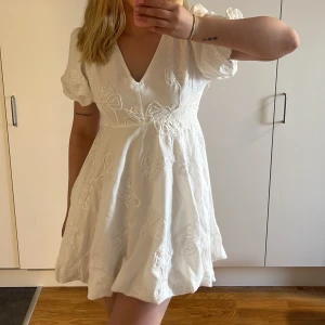 Vit kortklänning med broderade blommor - Superfin vit kortklänning med v-ringning och puffärmar. Klänningen har broderade blommor över hela tyget och en lätt utsvängd kjol. 💗💗