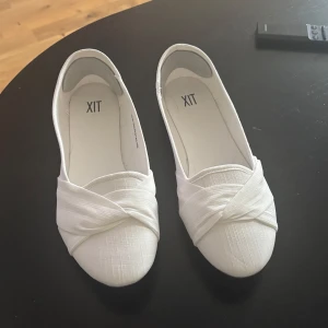 Vita ballerinaskor  - Snygga vita ballerinaskor från DinSko med korslagda detaljer framtill. Skorna har rund tå och platt sula i gummi. Ovandelen är i ett tyg med lätt struktur som ger en stilren och fräsch look. Perfekta för dig som gillar enkel och clean stil. Helt oanvända och nya 