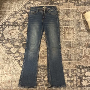 Blå bootcut jeans från Pull&Bear - Snygga blå bootcut jeans från Pull&Bear med klassisk femficksdesign och cool fickdetalj med knapp bak. Jeansen har en lätt utsvängd passform nertill och är gjorda i mjukt denimtyg. Perfekta för dig som gillar en retrovibe och vill ha ett par jeans som sticker ut.