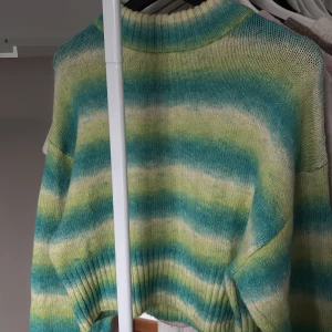 Randig stickad tröja från Gina Tricot - Supermysig stickad tröja från Gina Tricot med breda ränder i turkos, ljusgrön och vit. Tröjan har ribbad halsringning och muddar, samt en loose fit som ger en chill vibe. Perfekt för dig som gillar färg och vill sticka ut lite extra.