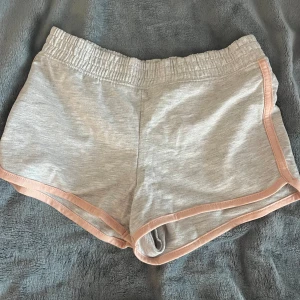 Grå shorts från H&M - Säljer ett par grå shorts från H&M med rosa kantdetaljer. De har en elastisk midja för extra komfort. Perfekta för en avslappnad stil.