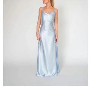 Ljusblå balklänning - Säljer nu min balklänning. Den är i satin med smala axelband och öppen rygg med knytning.  Det finns två band som man kan knyta där bak och ändra passformen vid midjan. Jag har bara användt den 1 gång förra året så den är i bra skick. Klänningen är slutsåld. NYPRIS 1450. 