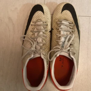 Nike fotbollsskor med snörning - Säljer ett par Nike fotbollsskor i vitt med svarta och röda detaljer. Skorna har snörning och en smidig design för optimal prestanda på planen. Perfekta för fotbollsträning och matcher.