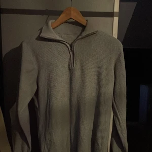 Grå tröja med dragkedja - Säljer en stilren grå tröja med dragkedja i halsen. Tröjan är tillverkad av återvunnen bomull och polyester, vilket gör den både bekväm och hållbar. Perfekt för kyligare dagar.