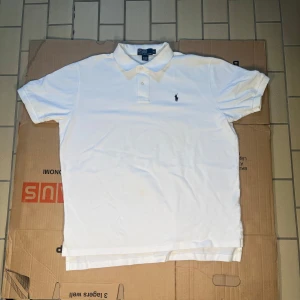 Vit kortärmad pikétröja från Ralph Lauren - Säljer en klassisk vit pikétröja från Ralph Lauren i storlek XL. Tröjan är tillverkad i 100% bomull och har en broderad logotyp på bröstet. Perfekt för en stilren och avslappnad look. Piken har en liten gul fläck (bild 5)! Om ni har några frågor svarar vi gärna på dem och priset kan såklart förhandlas 