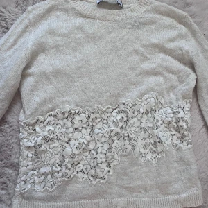 Vit stickad tröja med spetsdetalj - Säljer en vit stickad tröja med vacker spetsdetalj över magen. Tröjan har långa ärmar och en rund halsringning. Jättefiiin💕💕💕