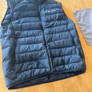 Sail racing väst svart - Säljer en svart dunväst från Sail Racing. Västen är i bra skick 10/10 och knappt använd storlek L.           Nypris 1800💸.                                                       Mitt pris 750kr ✅🔥.                                                       Hör av er vid eventuella frågor📲/Filip.                          ⁉️⚠️Tillägg den är hyfsad liten i storlek så den sitter nästan som en medium 📏