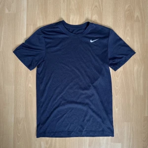 Mörkblå t-shirt från Nike - Säljer en stilren mörkblå t-shirt från Nike med korta ärmar och en vit Nike-logga på bröstet. Perfekt för träning eller en avslappnad dag. Skön och enkel design som funkar till det mesta.