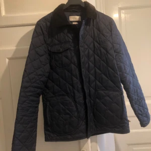 Blå quiltad jacka från These Glory Days - Snygg blå quiltad jacka från These Glory Days med krage i manchester. Jackan har långa ärmar och praktiska fickor framtill. Perfekt för våren, storlek L passar M, lite blekt på kragen 