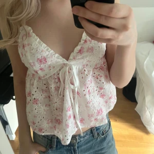 Vit blommig topp  - Söt vit topp med rosa blommönster och spetsdetaljer. Toppen har en v-ringad design och knytning framtill. Perfekt för sommaren! Aldrig använd🤗
