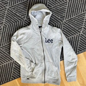 Grå hoodie från Lee - Säljer en grå hoodie från Lee med dragkedja och justerbar huva. Riktigt skön tröja!! Perfekt för en avslappnad stil.