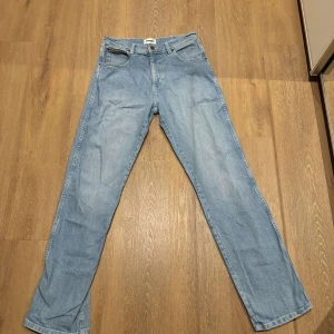 Blå jeans från Wrangler - Säljer ett par klassiska blå jeans från Wrangler. De har en straight passform och är tillverkade i jeansmaterial. Perfekta för dig som precis kollat på Yellow stone och vill se ut som en av dem. Jeansens baksida har Wrangler-loggan på bakfickan. W30 L32 och ny pris ligger på 899kr