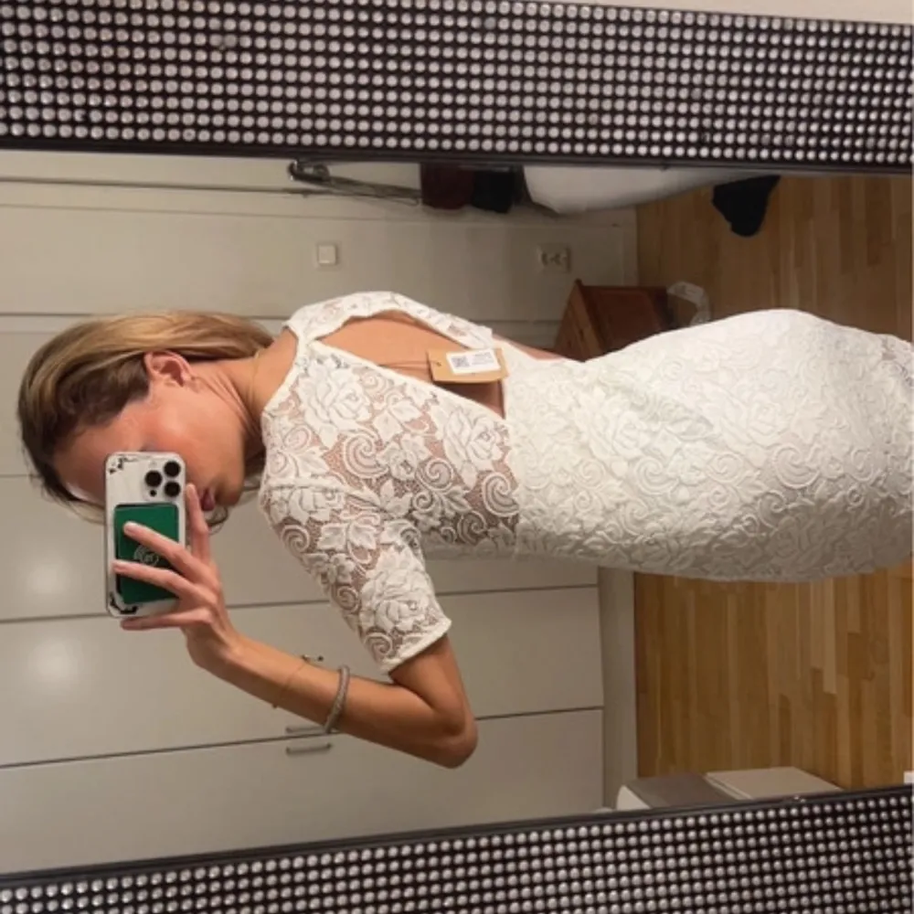 Elegant vit spetsklänning med korta ärmar och v-ringning. Klänningen har en vacker öppen rygg och är i en kort modell. Perfekt för sommarens festligheter.. Mekot.