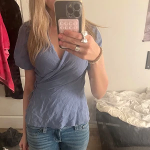 Blå omlottopp - Säljer en söt blå omlottopp med korta ärmar och knytband i sidan. Toppen har en v-ringad design och är gjord i ett lätt material. Nästan aldrig använd🩷